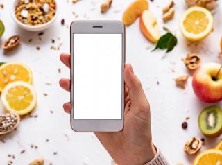 Female hands holding smartphone on healthy food background.