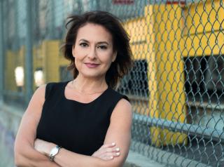 A portrait image of Shari Bayer with her arms crossed standing in front of a fence.