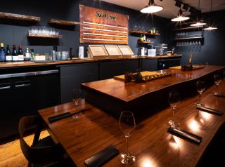 A restaurant dining room with a wooden table, wine glasses, and dark blue walls.